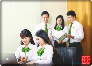 Mẫu đồng phục vietcombank với áo sơm mi trắng trắng dài tay kết hợp thắt nơ cách điệu màu xanh dành cho các giao dịch viên nữ